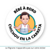 Ce sticker rond illustre une petite fille à la peau blanche avec des cheveux bruns courts. Elle porte une robe blanche à rayures bleues ornée d’un petit cœur rouge sur le devant. Dans sa main droite, elle tient un moulin à vent multicolore. Le texte "Bébé à Bord" est inscrit en haut, tandis que "Chichou en la Carreta", en Niçois, apparaît en bas en noir. Sticker bébé à bord. 
